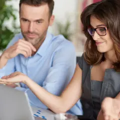 Kobieta w okularach i mężczyzna patrzą na laptopa, omawiając coś.