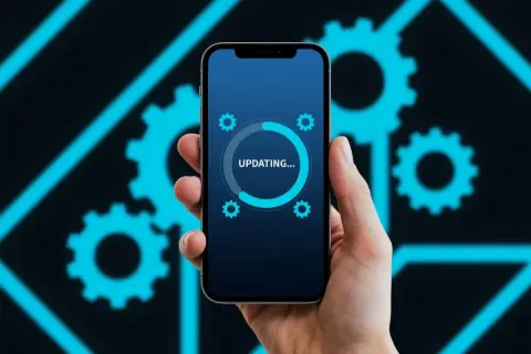 Dłoń trzyma smartfon z ekranem aktualizacji systemu Android na tle niebieskich kół zębatych.